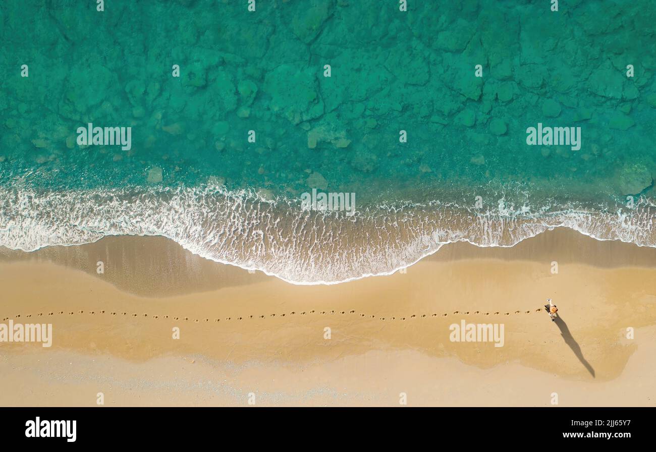 Frau geht am Strand entlang brechender Wellen und hinterlässt Spuren auf dem Sand. Luftaufnahme direkt darüber Stockfoto