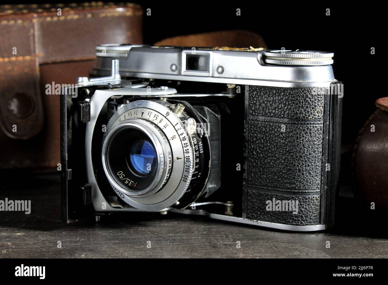 Eine deutsche Kamera aus dem Jahr 1950s mit einem Lederetui auf einem dunklen Holztisch und schwarzem Hintergrund Stockfoto