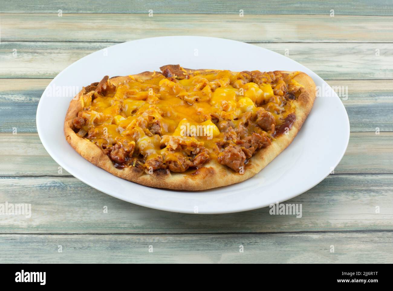 Hausgemachte Fladenbrot-Pizza mit Käse auf weißem Teller mit Ananas und Schweinefleisch auf dem Tisch Stockfoto