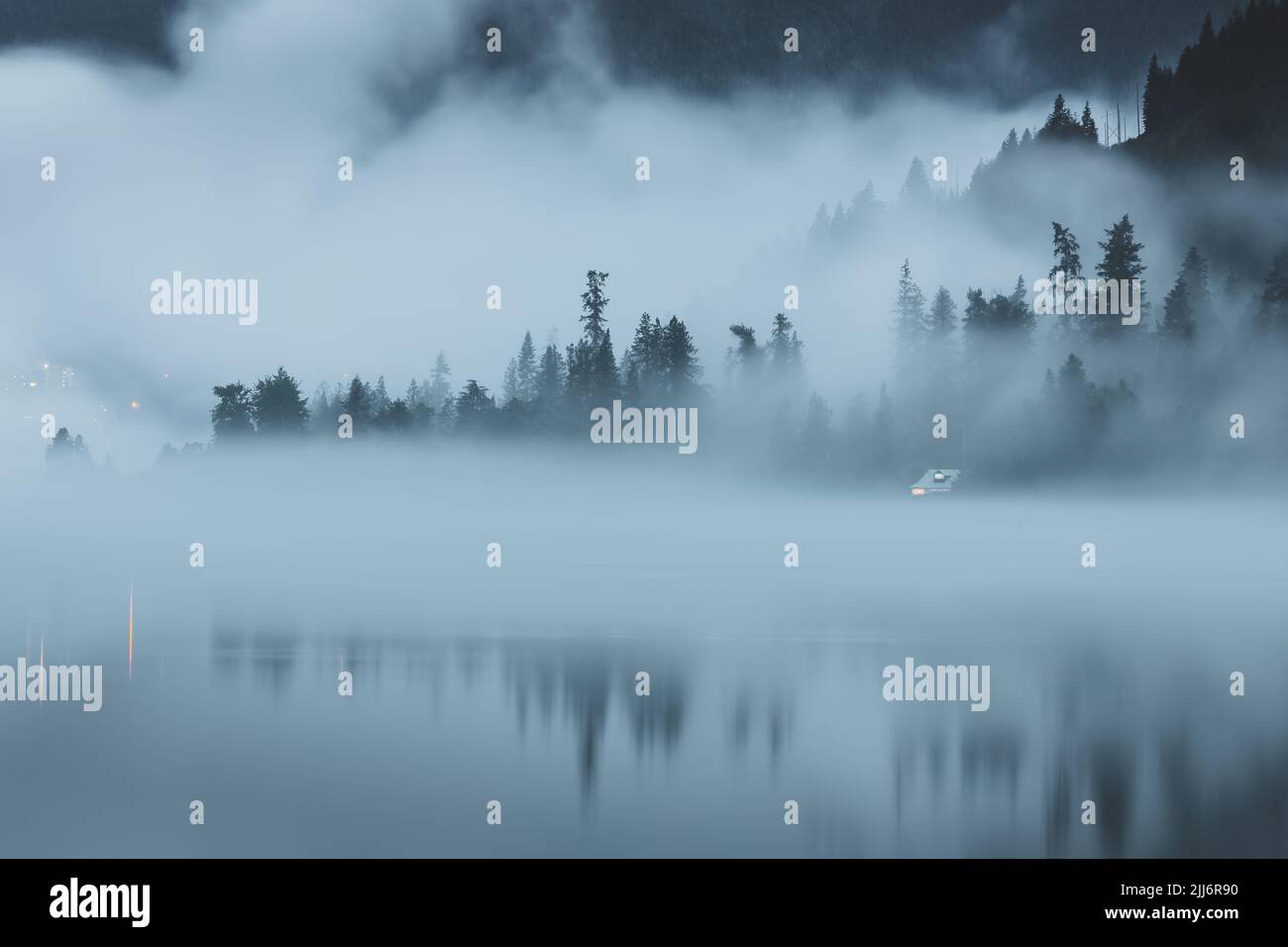 Stimmungsvoller Abendnebel über dem Kootenay Lake in Nelson, BC, Kanada, mit einer abgelegenen, abgeschiedenen Hütte am Wasser. Stockfoto