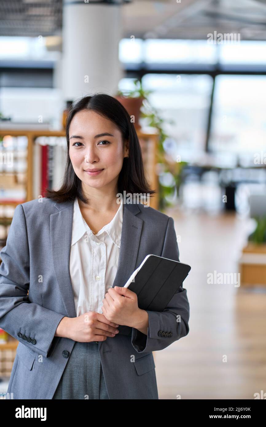 Lächelnde junge asiatische Geschäftsfrau, die im Büro steht. Vertikales Hochformat Stockfoto