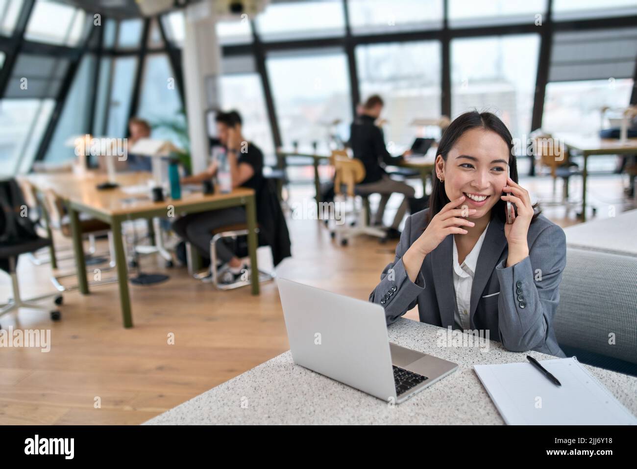 Junge glückliche asiatische Geschäftsfrau trägt Anzug arbeiten in großen modernen Büro. Stockfoto