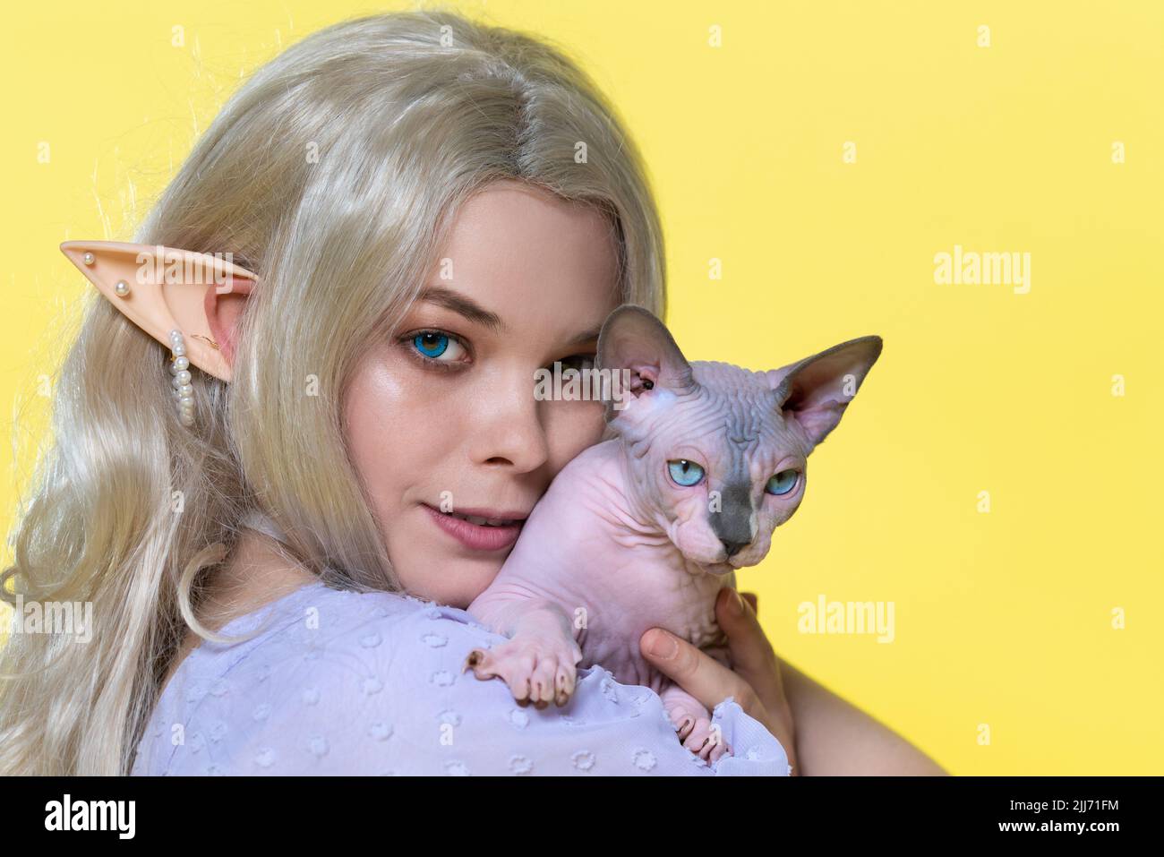 Porträt einer jungen Frau, die die Sphinx-Katze in der Nähe der Wange hält. Elfe im sommerblauen Kleid, mit schönen blonden lockigen langen Haaren Stockfoto