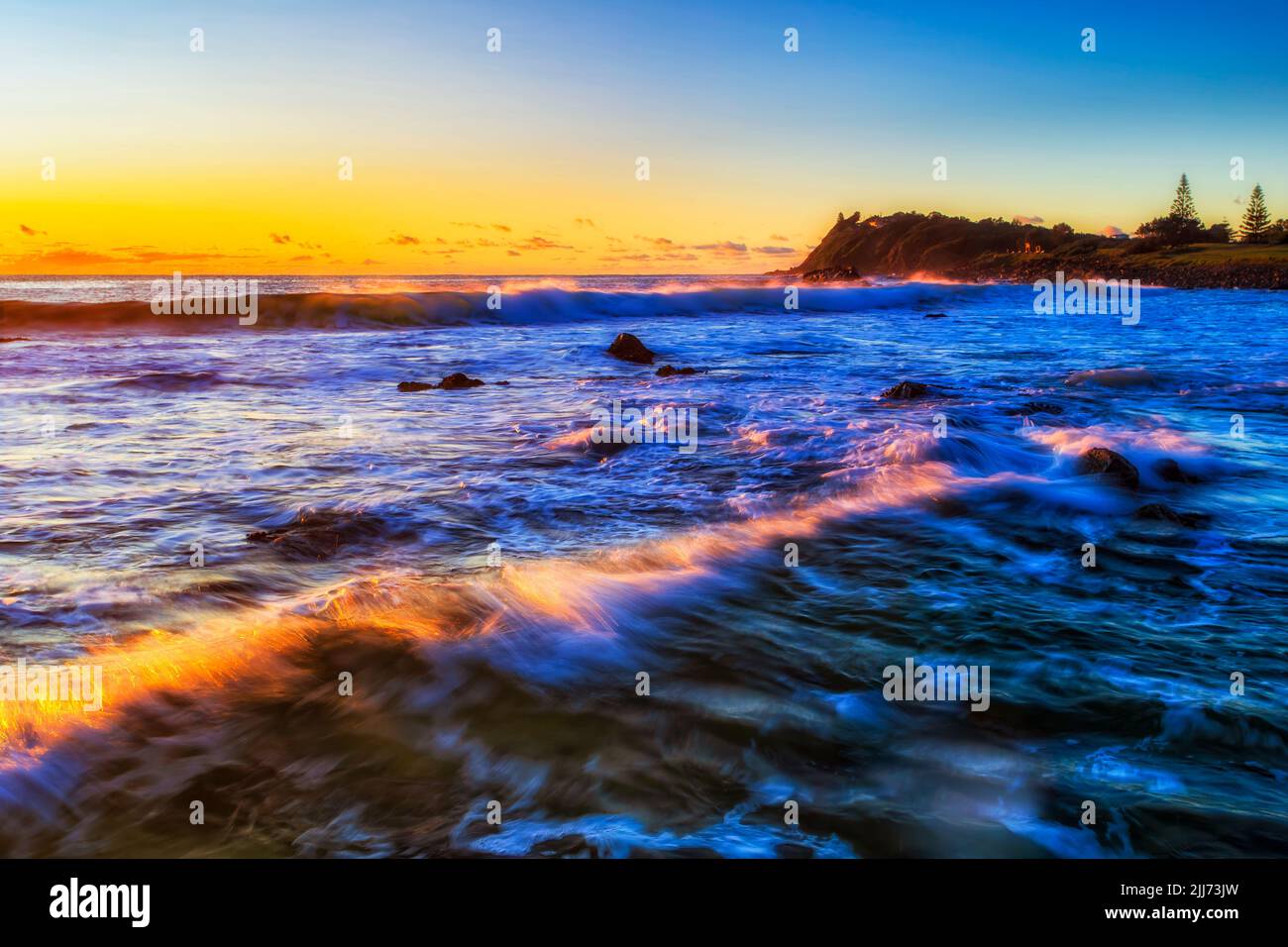 Sonnenlicht auf Wellen rollender Wellen am Kiesstrand in Forster, der australischen Stadt, bei Sonnenaufgang - Meereslandschaft. Stockfoto