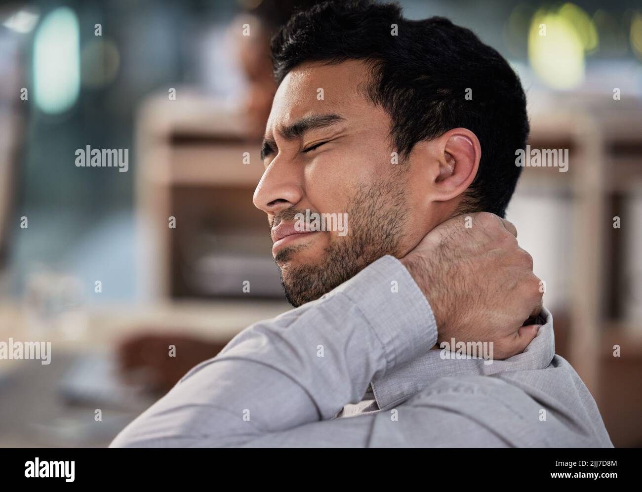 Ich saß den ganzen Tag gebeugt und ein hübscher junger Geschäftsmann saß allein in seinem Büro und litt unter Nackenschmerzen. Stockfoto