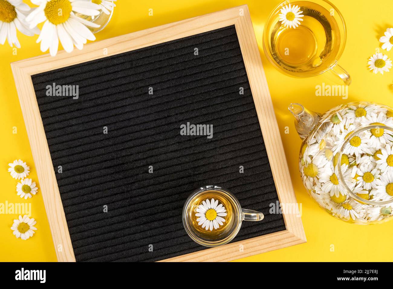 Leuchtender Sommer im Nachbau. Leere leere schwarze Brieftafel und Kräuterkamillentee auf gelbem Hintergrund. Layoutvorlage Für Nachbau. Stockfoto