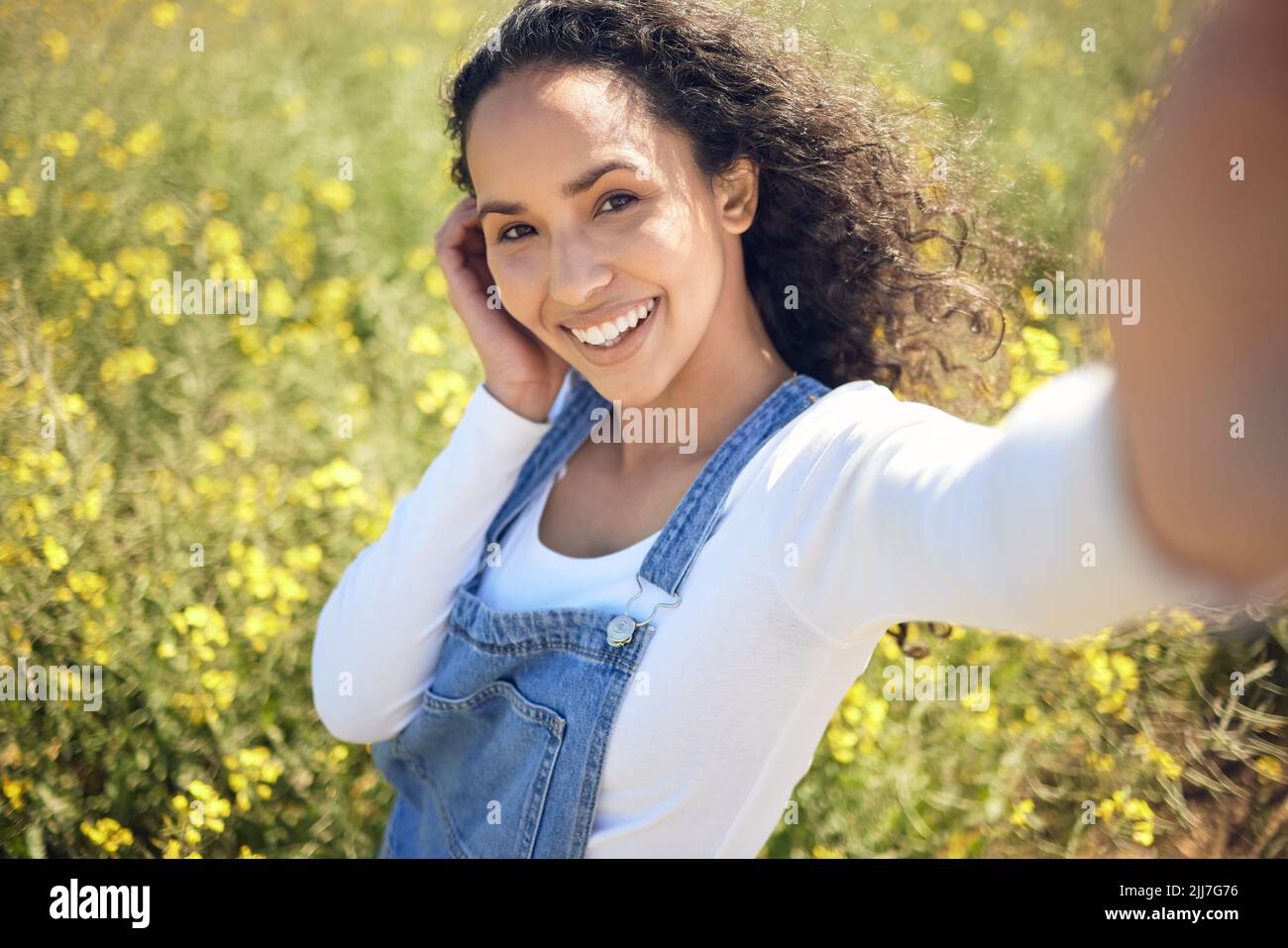 Jeder kennt mich als das schöne Landmädchen. Eine junge Frau, die ein Selfie gemacht hat, während sie von gelben Blumen umgeben ist. Stockfoto