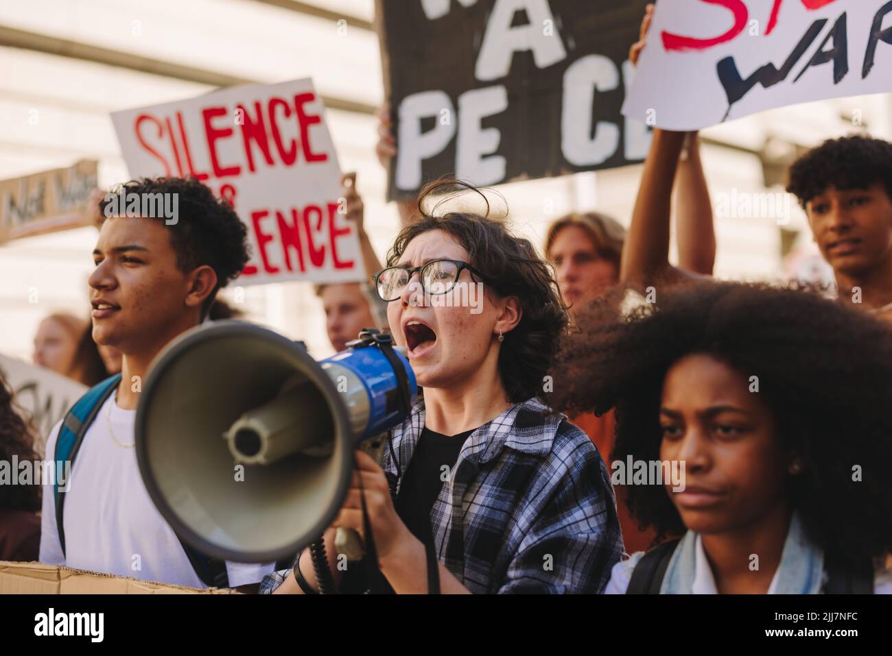 Multikulturelle Jugendaktivisten protestieren in den Straßen der Stadt gegen Krieg und Gewalt. Eine Gruppe von Demonstranten der Generation Z, die Slogans und Rais singen Stockfoto