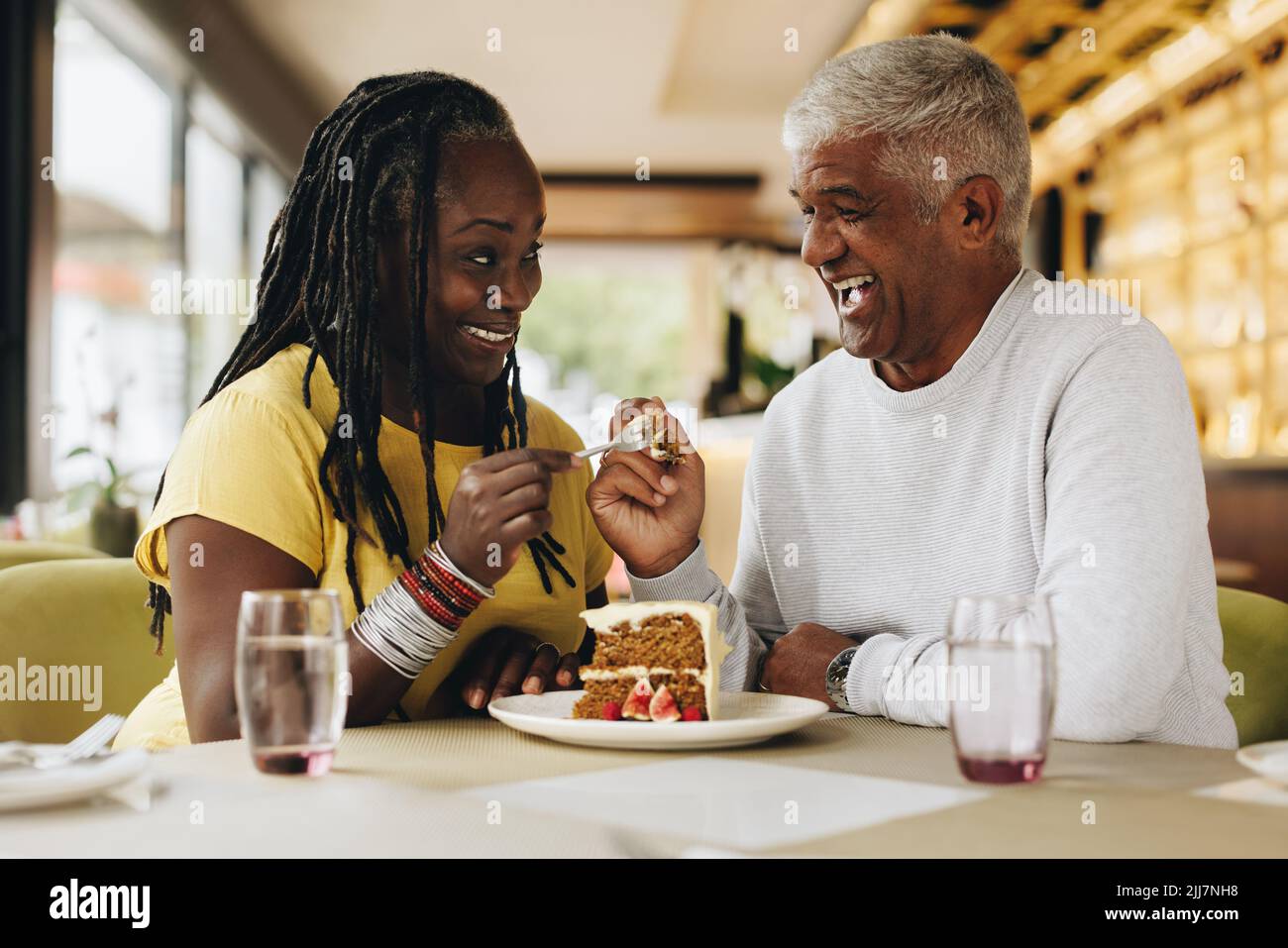 Ältere Paare lächeln einander an, während sie einen leckeren Kuchen in einem Café teilen. Glückliches Seniorenpaar, das eine gute Zeit in einem Restaurant hatte. Fröhlich reif Stockfoto