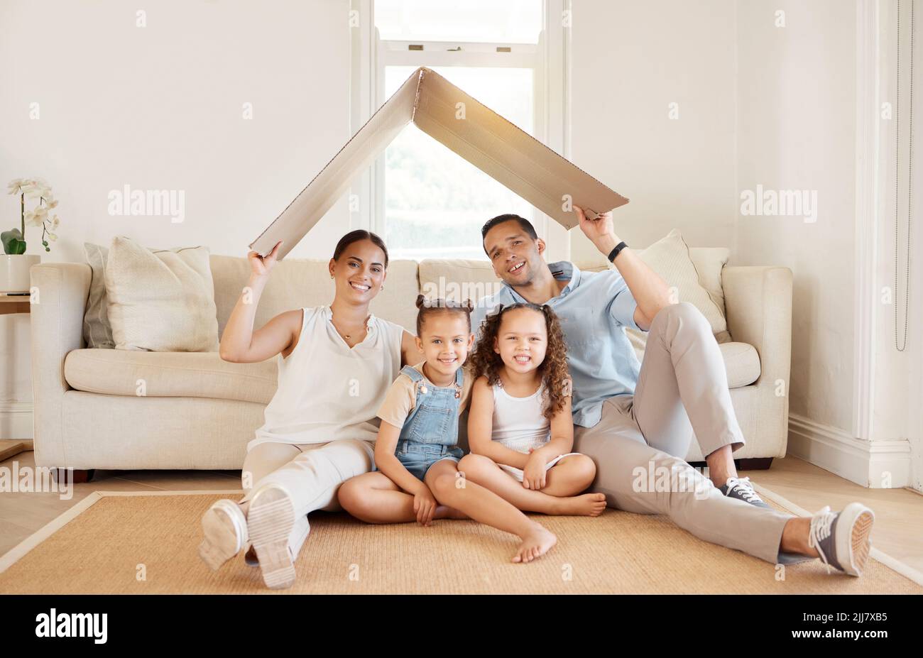 Ein Haus besteht aus Liebe und Träumen. Eine junge Familie hält einen Karton, um ein Dach über dem Kopf zu bilden. Stockfoto