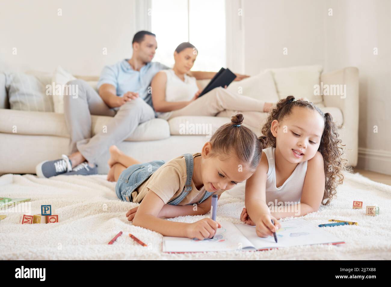 Mit einem Geschwister bedeutet, dass Sie immer einen Spielkameraden haben. Zwei kleine Mädchen, die Kunstwerke machen, während ihre Eltern im Hintergrund sitzen. Stockfoto