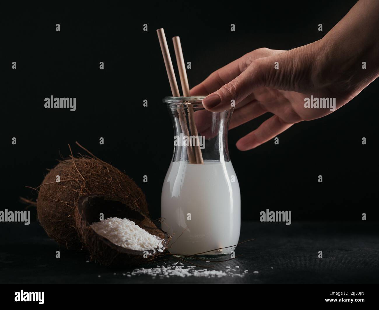 Flasche Kokosnuss vegane Milch mit Trinkhalmen, Kokosnuss und Flocken auf schwarzem Hintergrund Stockfoto