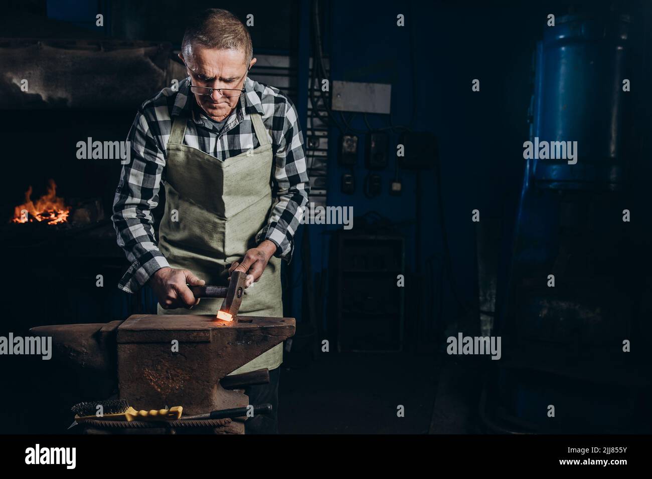 Der Schmied schmiedet das rotglühende Metall manuell auf dem Amboss in der Schmiede. Harte Arbeit. Energie und Leistung. Konzept der Arbeit, Retro-Berufe Stockfoto