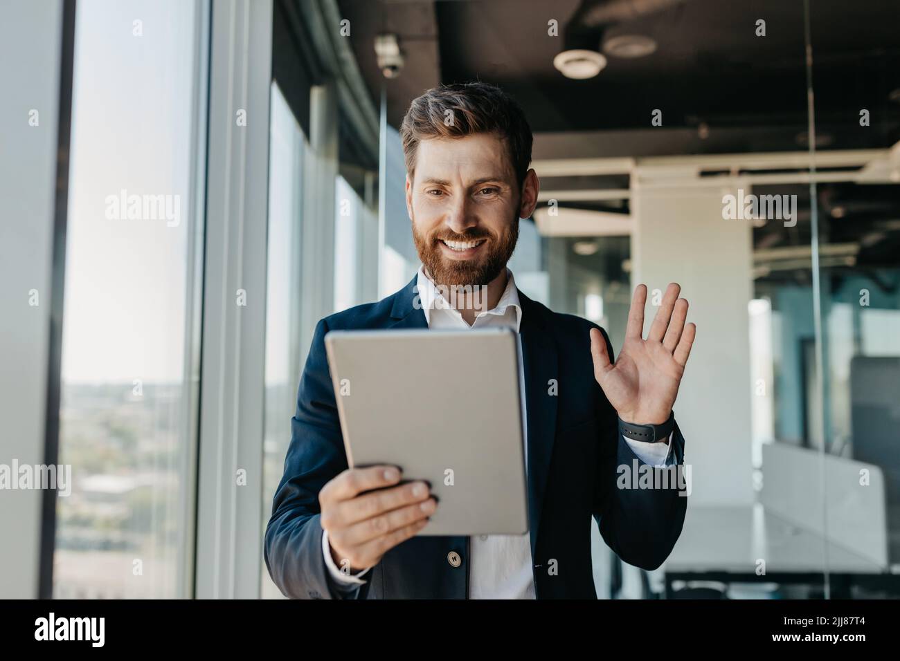 Glücklicher kaukasischer Geschäftsmann im Anzug, der im Büro arbeitet, mit Geschäftspartnern über ein digitales Tablet chatten kann Stockfoto