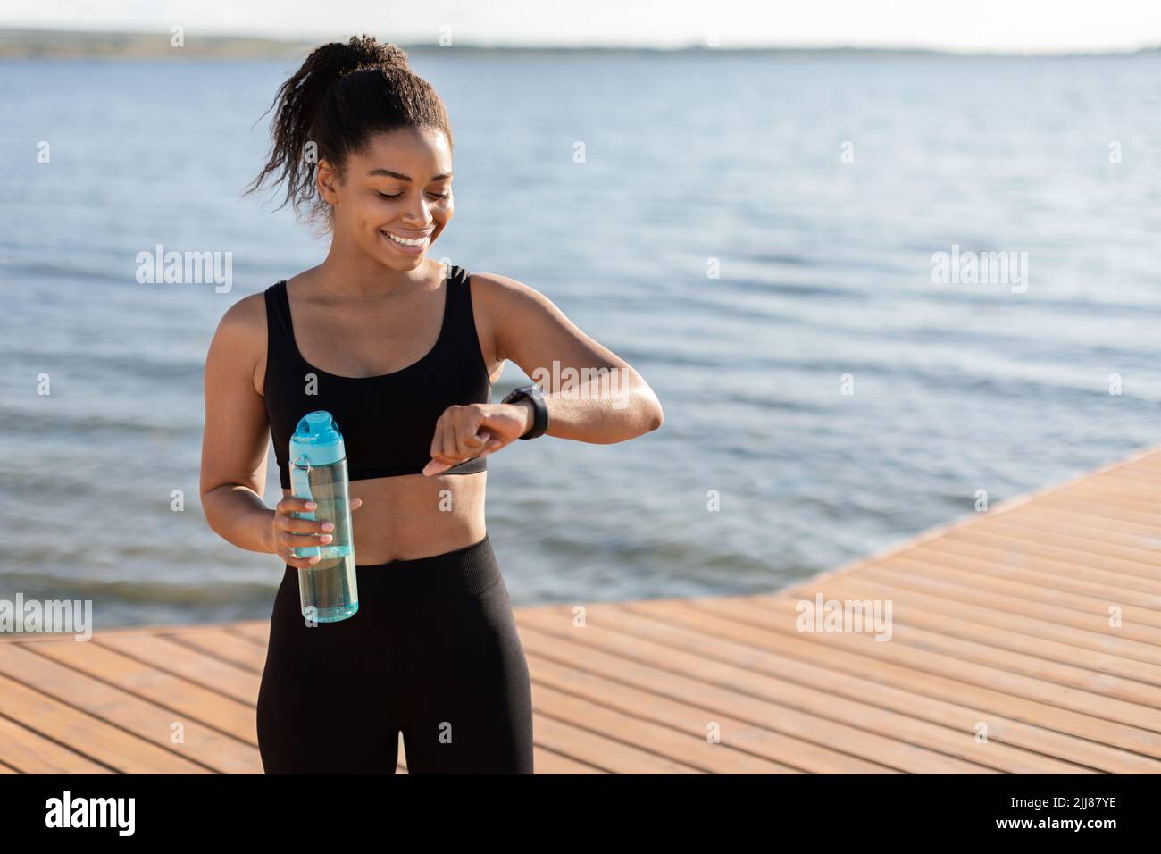 Athletische schwarze Frau Trinkwasser, Überprüfung Fitness-Armband Stockfoto