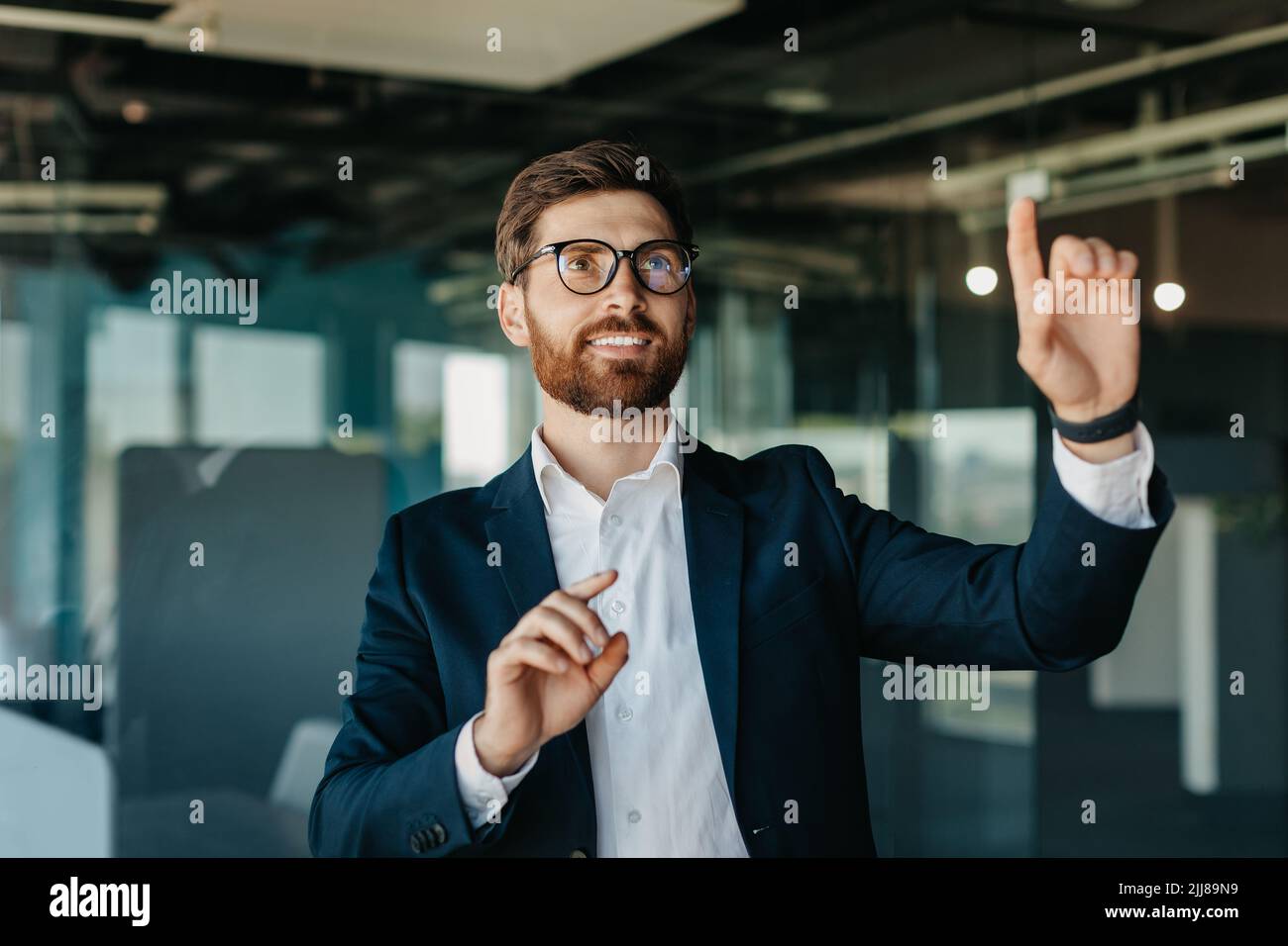 Erfolgreicher Unternehmer in formalwear Auswahl etwas auf virtuellen Bildschirm, stehend in modernen Büroinnenraum, mockup Stockfoto