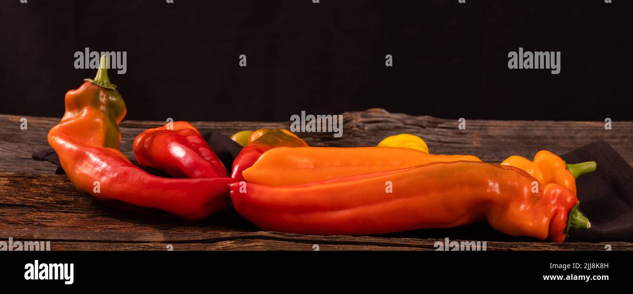 Rote, orange und gelbe lange Paprika auf einem alten rustikalen Holztisch Stockfoto