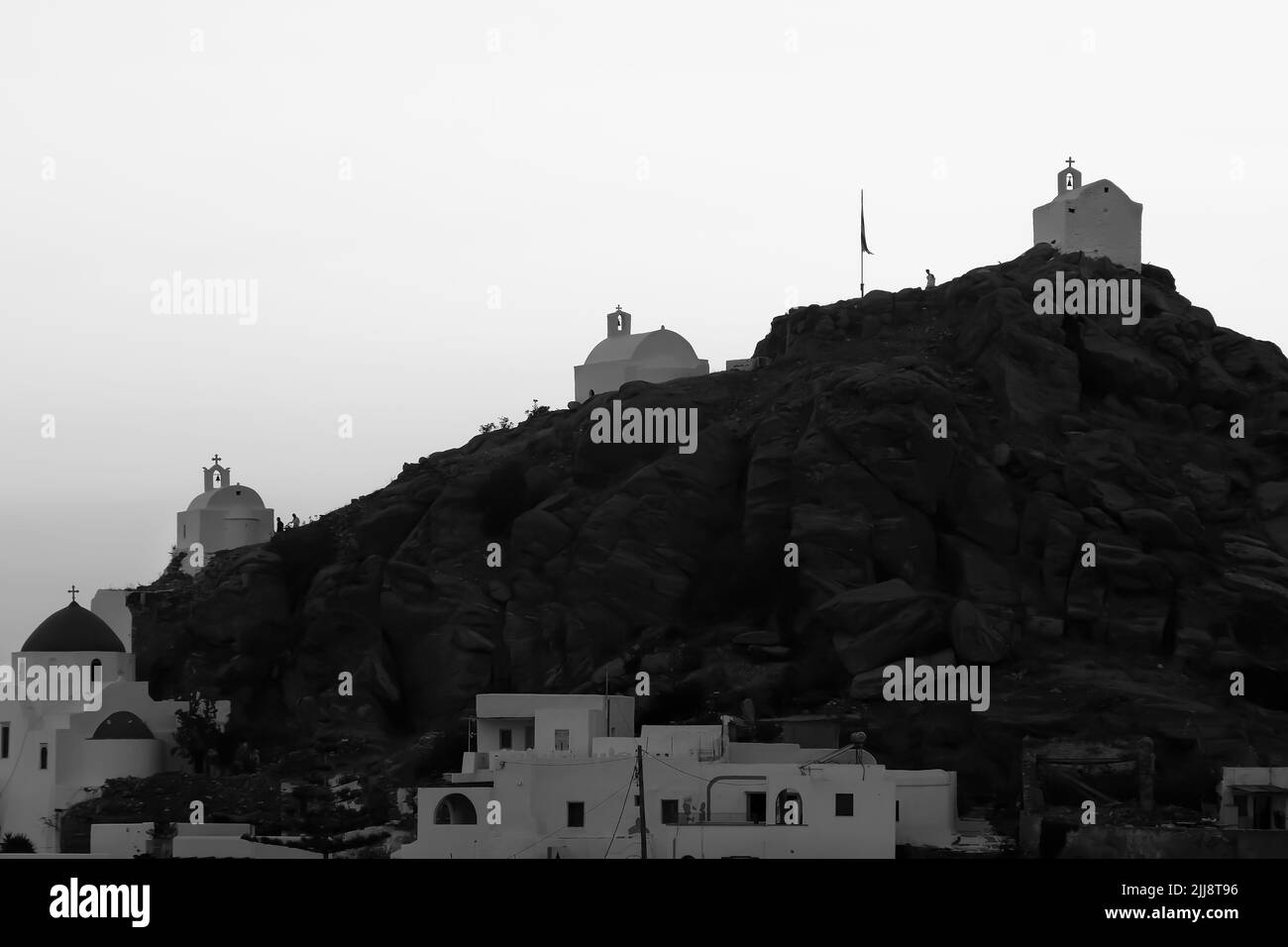 Touristen erkunden die malerischen kleinen Kapellen auf der atemberaubenden Insel iOS Greece, während die Sonne schwarz-weiß untergeht Stockfoto