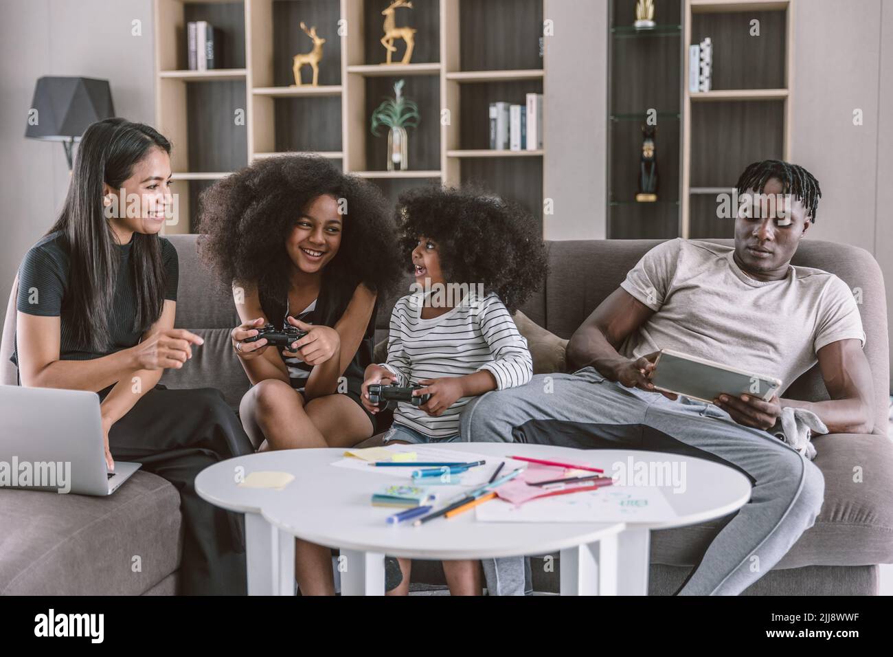 Entspannen Sie fröhliche multirassische Familie, Eltern mit zwei Kindern sitzen auf dem Sofa Wohnzimmer spielen Videospiel Freizeit Urlaub zusammen. Stockfoto