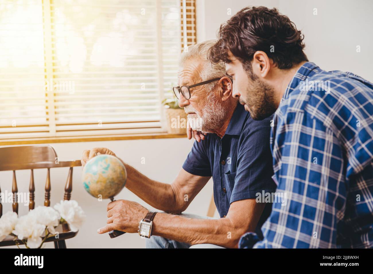 Der ältere Onkel erzählt seinem Sohn im Pass die Geschichte eines Weltabenteuers und zeigt auf das Land der Distination, im Kartenmodell zu Hause. Stockfoto