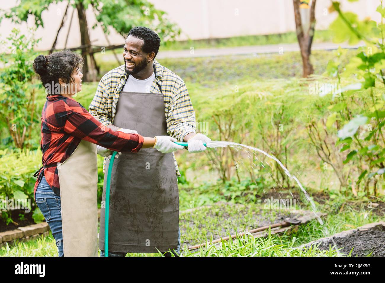 Schönes Paar schwarzen Mann mit Frau Menschen Bewässerung Pflanze im Garten glücklich lächelnd zusammen. Stockfoto