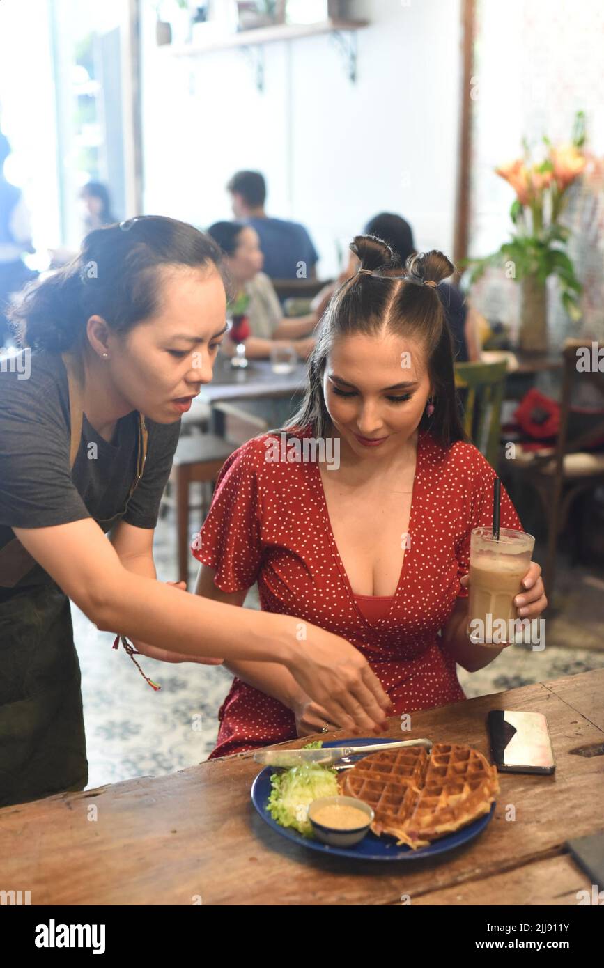 Vietnamesische Kellnerin servierte einer kaukasischen Frau Waffeln Stockfoto
