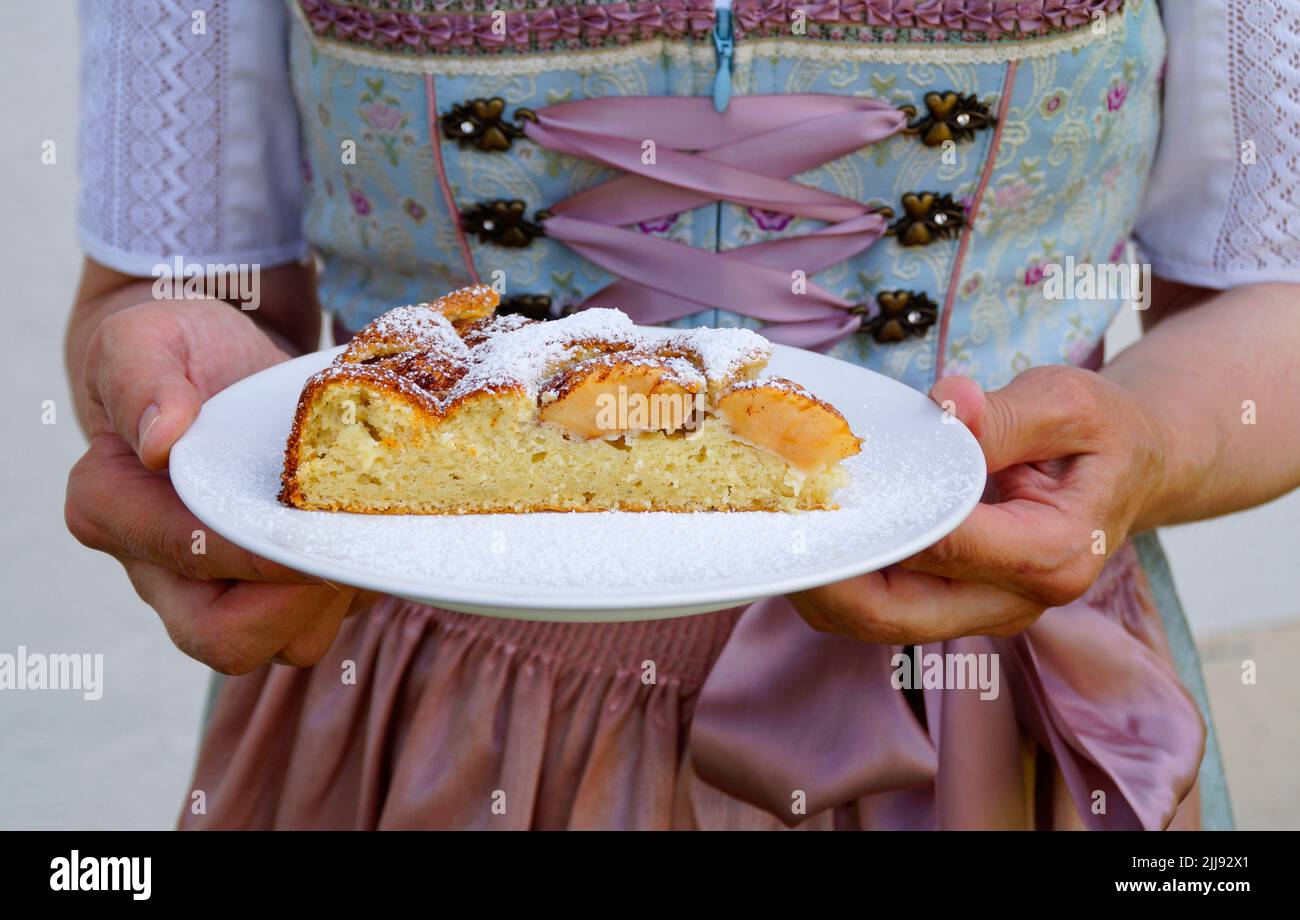 Eine Frau in einem schönen traditionellen Dirndl-Kleid mit einem Stück köstlichem hausgemachten Apfelkuchen auf dem Oktoberfest (Bayern, Stockfoto