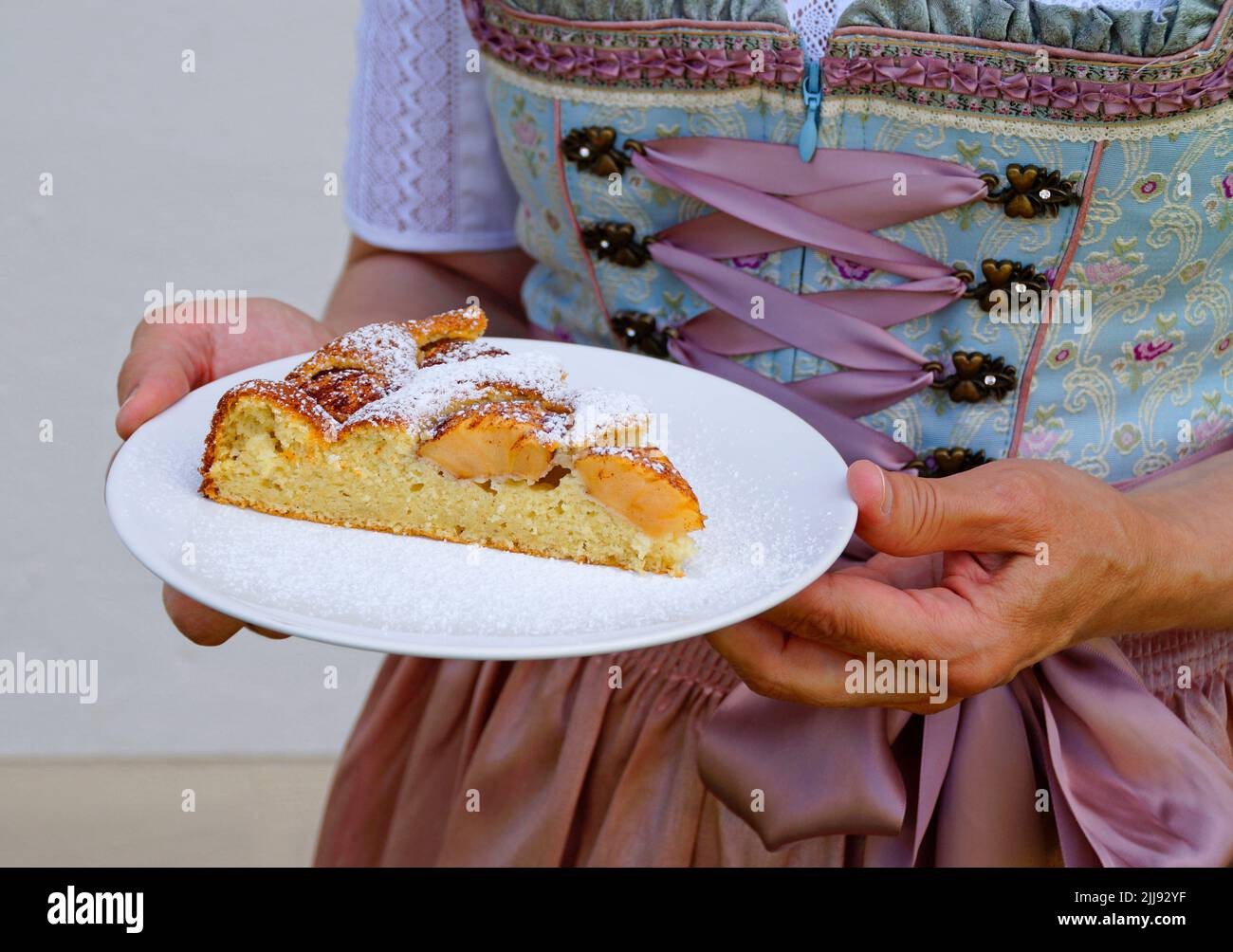 Eine Frau in einem schönen traditionellen Dirndl-Kleid mit einem Stück köstlichem hausgemachten Apfelkuchen auf dem Oktoberfest (Bayern, Stockfoto