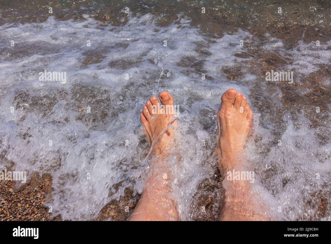Nahaufnahme der männlichen Beine an der Küste während der rollenden Welle. Konzept für Sommerferien. Stockfoto