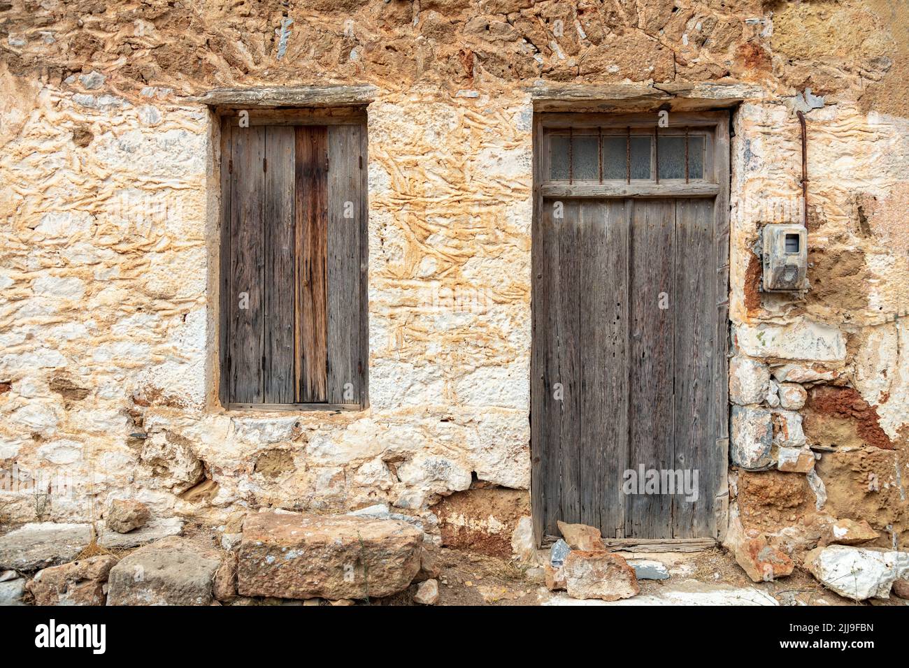 Alte traditionelle ländliche Haus Fassade Hintergrund. Verwitterte Steinmauer Hütte außen mit Holz braun geschlossen Fenster und Tür. Griechenland, Jahrgang aufgegeben Stockfoto