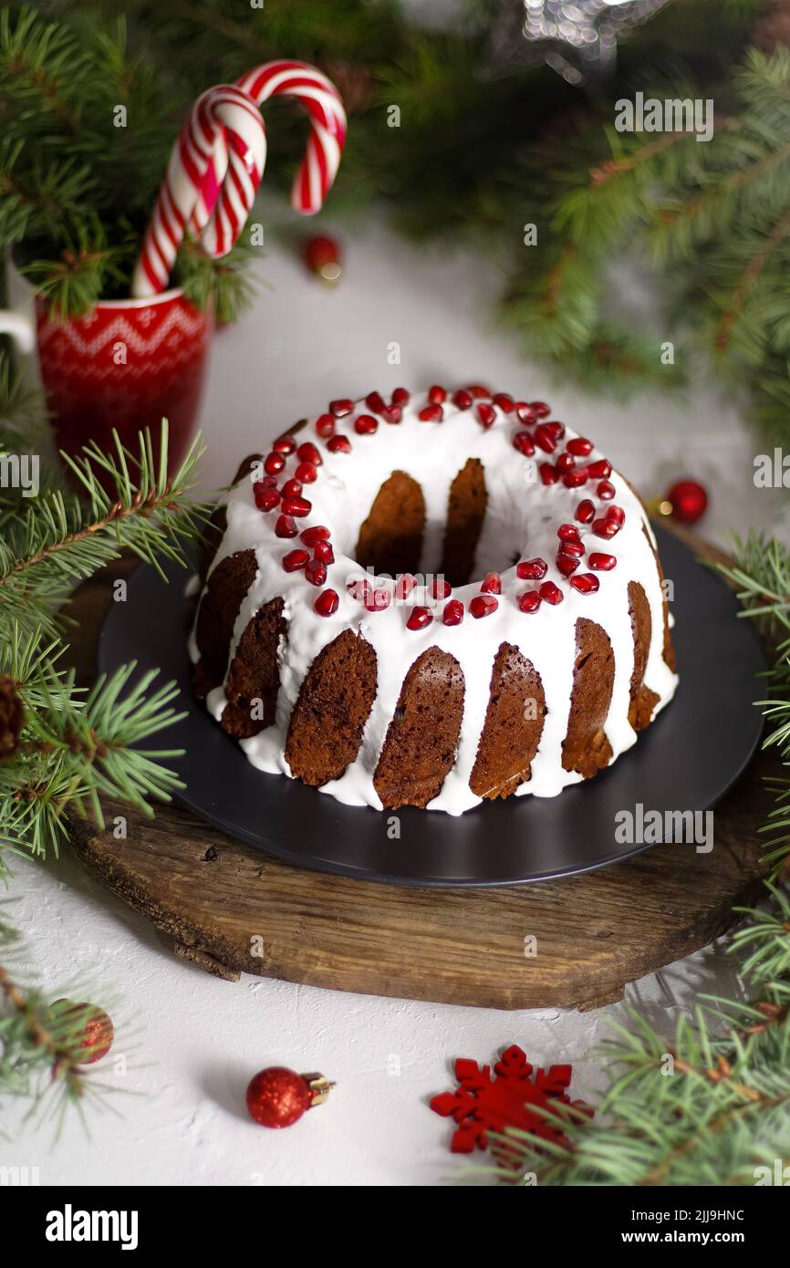 Weihnachtliches Essen. Runde Torte mit weißer Glasur. Cupcake mit einem Loch in der Mitte mit Granatapfel. Grüne Fichtenzweige auf dem Tisch. Stillleben. Süßes Gebäck, Desserts und Leckereien für das neue Jahr. Stockfoto
