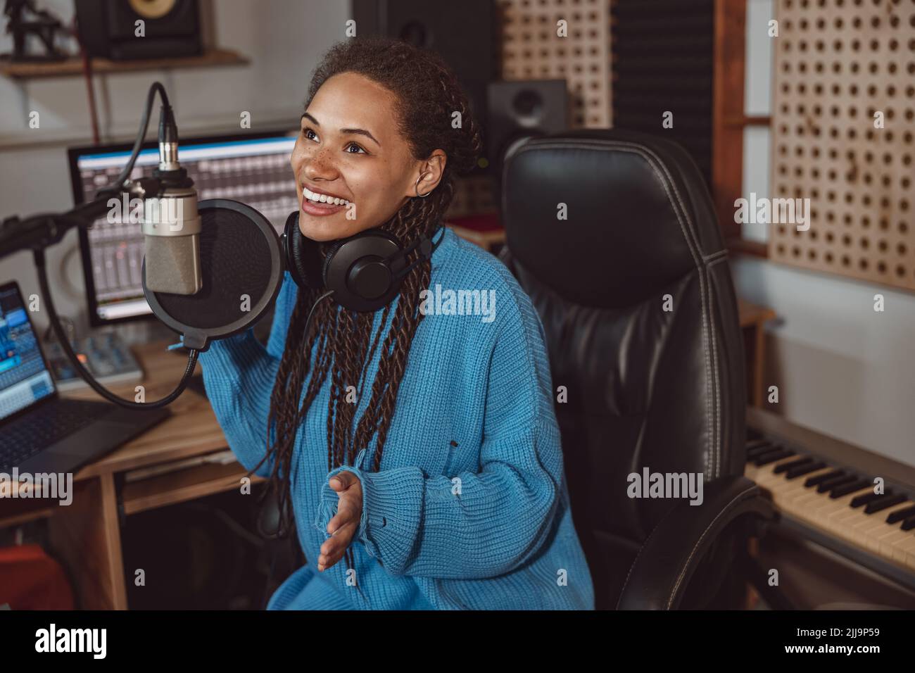 Afrikanische nette Bloggerin nimmt Podcast mit Kopfhörern auf und spricht im professionellen Musikstudio ins Mikrofon Stockfoto