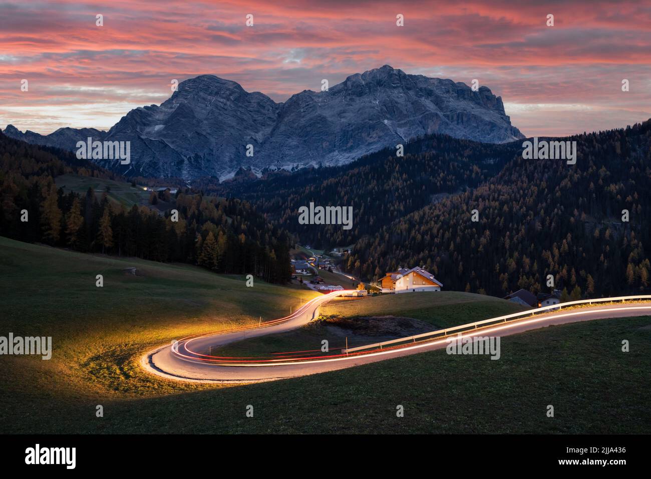 Glühende Straße in den herbstlichen Dolomiten. Atemberaubende Landschaft mit Lichtstraße und verschneiten Bergen im Hintergrund in St. Genesio, Provinz Bozen, Südtirol, Italien Stockfoto