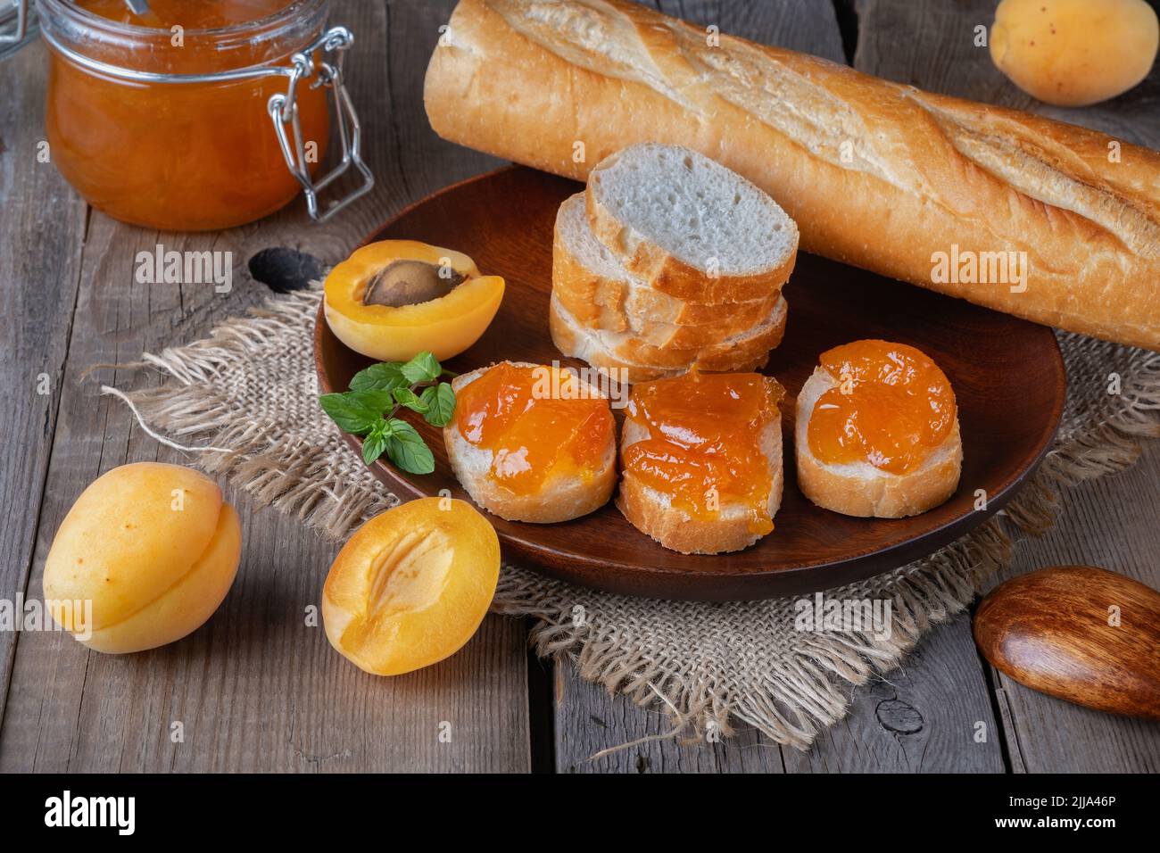 Toast mit Aprikosenmarmelade und frischen Früchten mit Minze auf einem Holztisch. Stockfoto