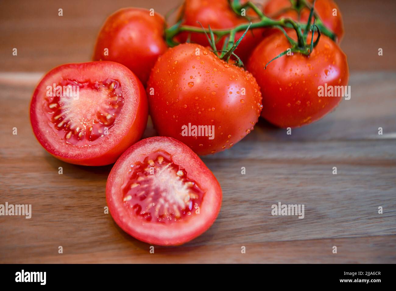 Rote Tomaten auf Weinrebe in der Küche - geschnittene und ganze frische Tomaten auf Holzschneidebrett - reife Solanum lycopersicum Bunch und Cluster Stockfoto