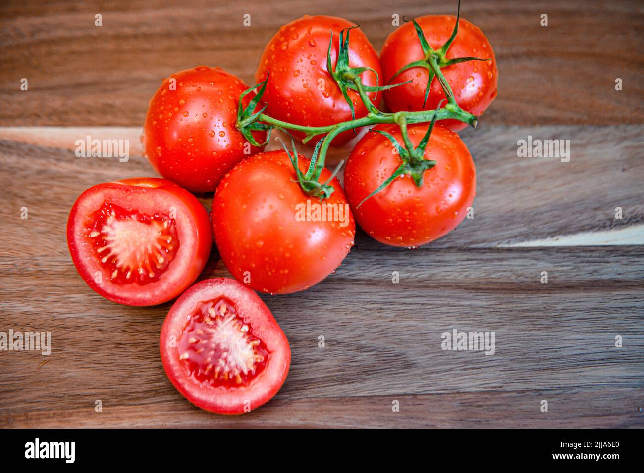 Rote Tomaten auf Weinrebe in der Küche - geschnittene und ganze frische Tomaten auf Holzschneidebrett - reife Solanum lycopersicum Bunch und Cluster Stockfoto