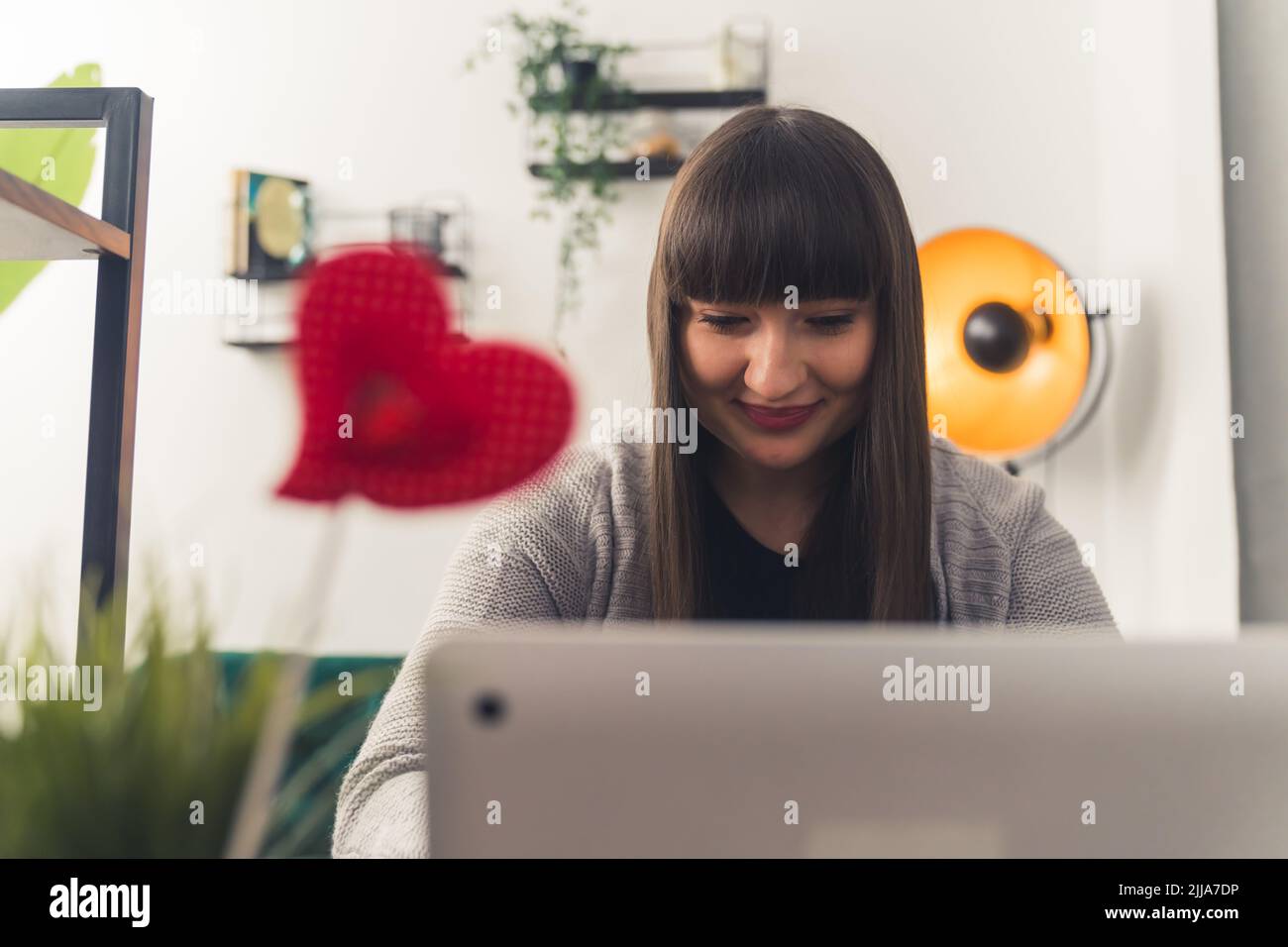 Lächelnde weiße Frau mit dunklen Haaren und knallt in bequemen Kleidern, die auf einem Laptop im Wohnzimmer arbeiten. Innenaufnahme. Hochwertige Fotos Stockfoto