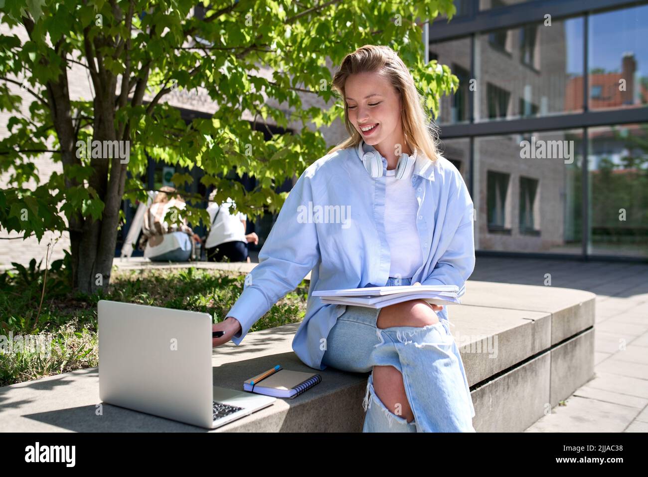 Lächelnde Studentin mit Laptop, die im Freien auf dem Universitätscampus studiert. Stockfoto