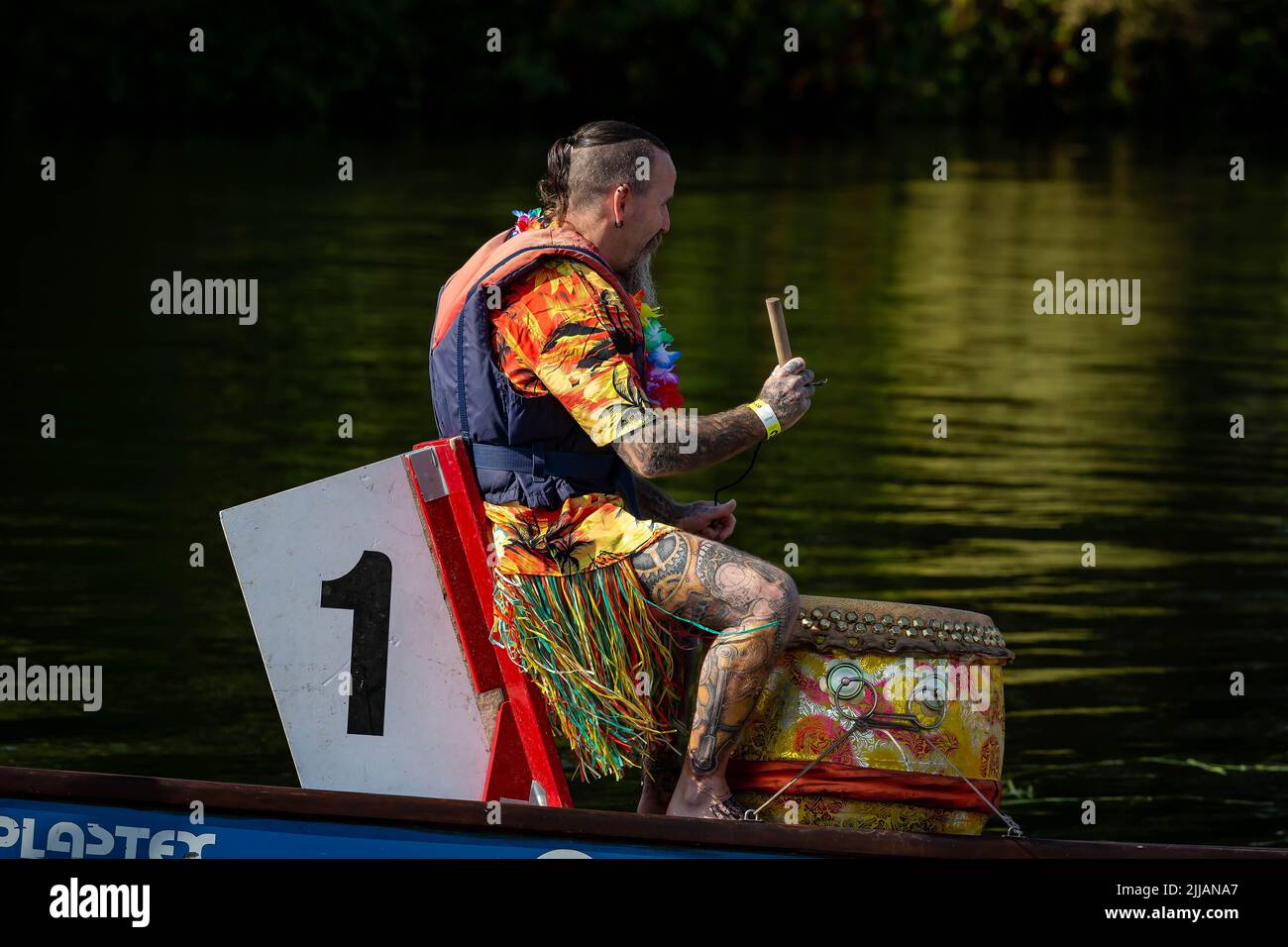 Mann in Hawaiiihemd und Grasrock schlägt bei einem Drachenboot-Rennen auf die Trommel Stockfoto