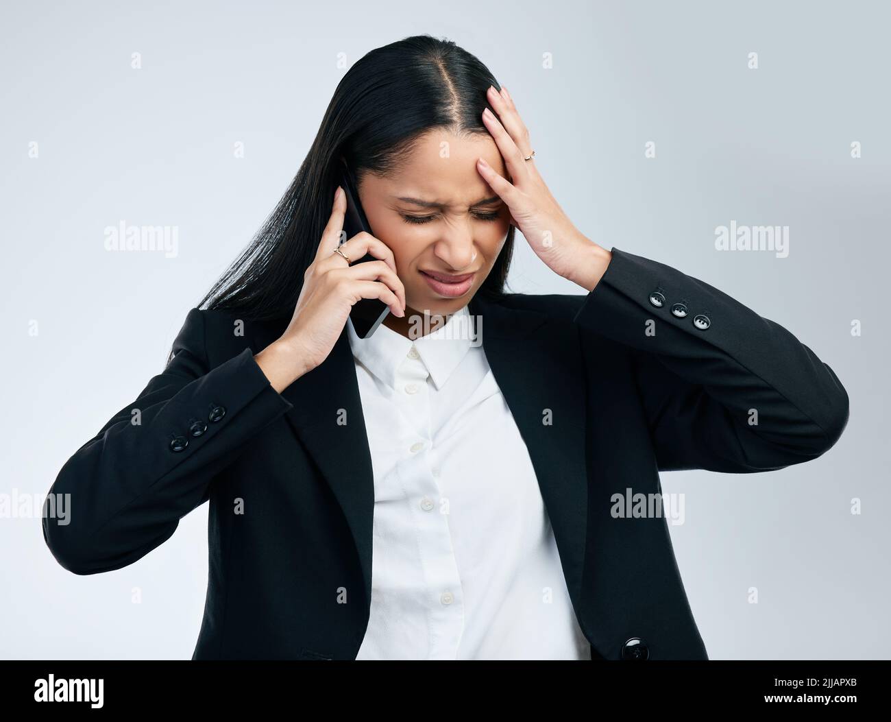 Geld kostet oft zu viel. Eine junge Geschäftsfrau benutzt ein Telefon vor grauem Hintergrund. Stockfoto
