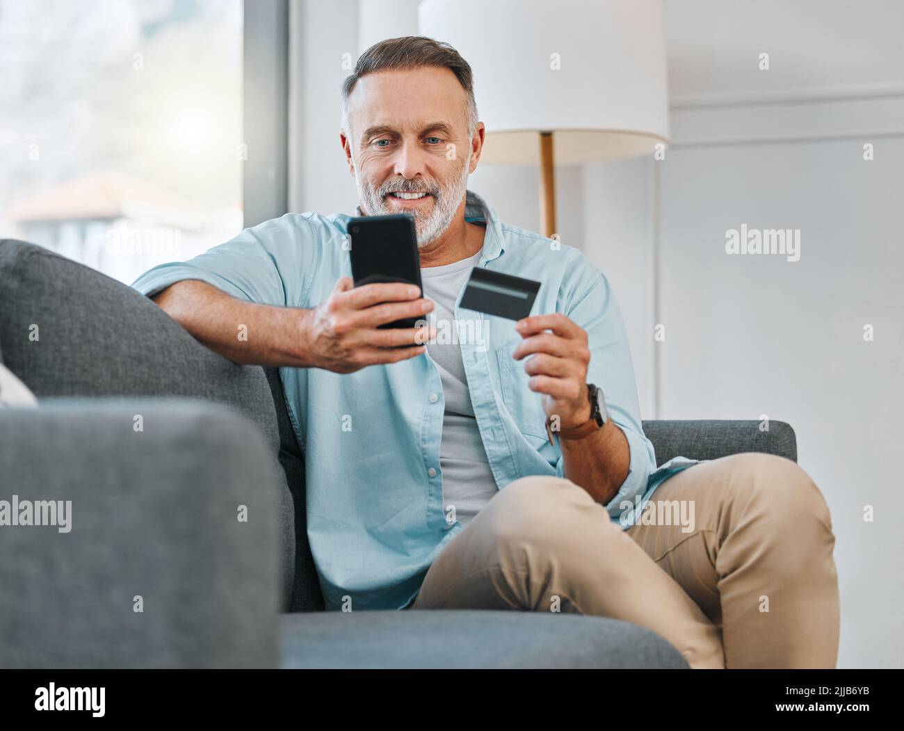Ja, es ist immer noch verfügbar. Ein reifer Mann sitzt allein auf seinem Sofa zu Hause und nutzt sein Handy zum Online-Shopping. Stockfoto