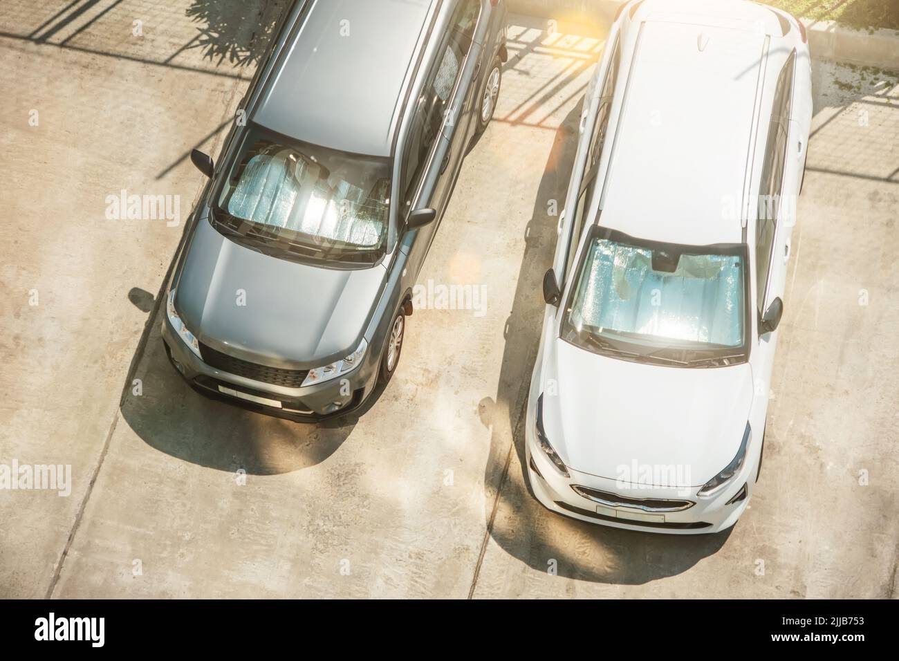 Reflektierende Schutzfläche unter der Windschutzscheibe der silbernen und weißen Autos der Beifahrer, die an einem heißen Tag geparkt und durch die Sonnenstrahlen im Auto beheizt wurden Stockfoto