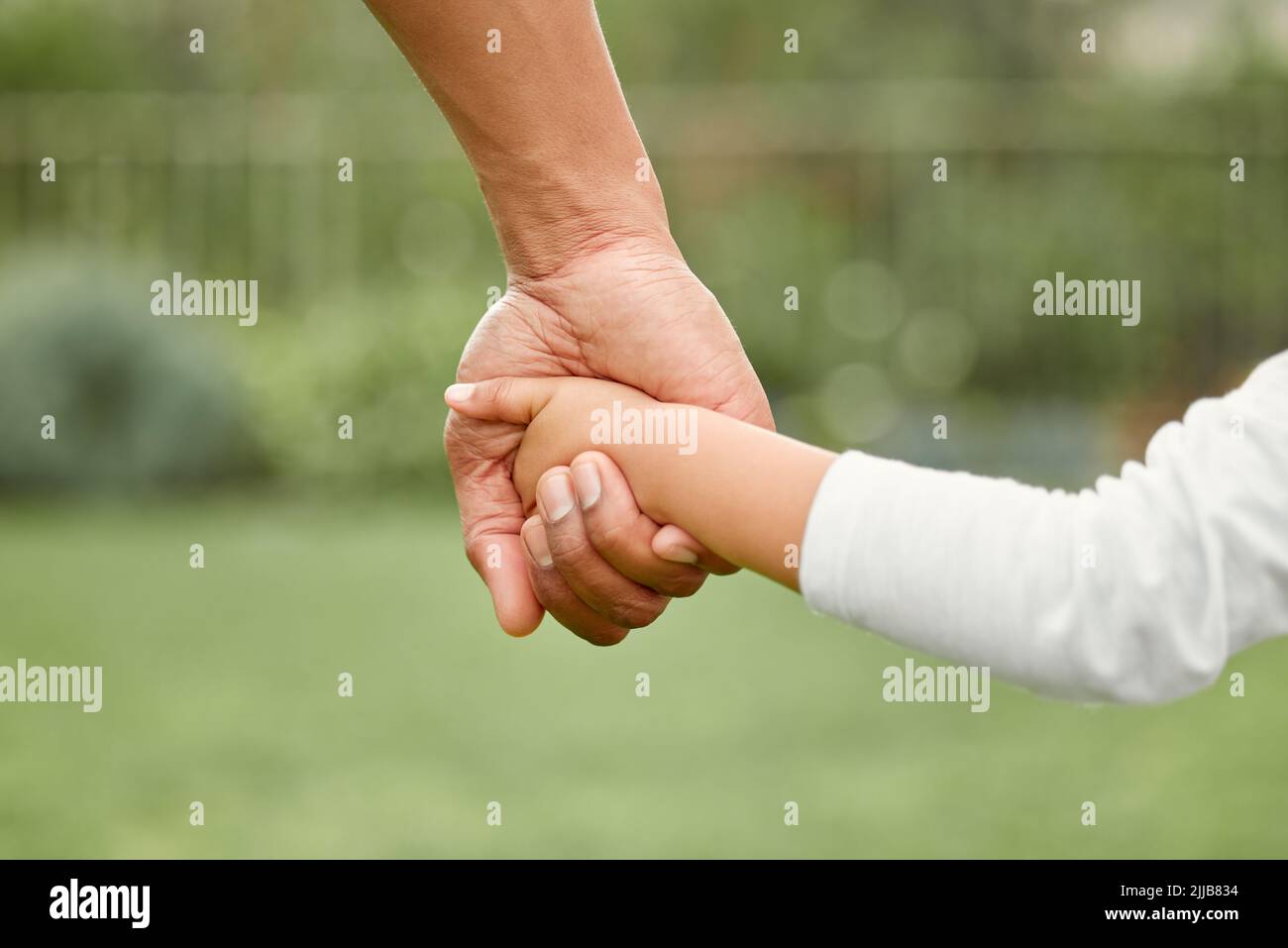 Eine unterstützende Familie baut ein Zuhause. Ein kleines Mädchen hält ihre Väter in der Hand, während es im Park spazieren geht. Stockfoto