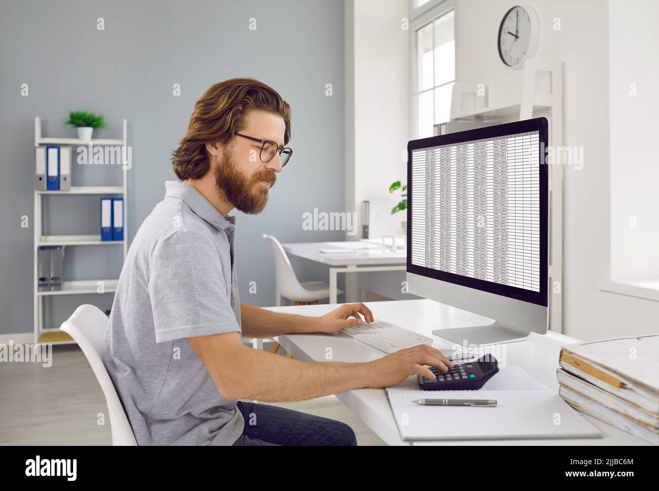 Wirtschaftsprüfer sitzt am Bürocomputer, arbeitet mit Kalkulationstabellen und mit Taschenrechner Stockfoto