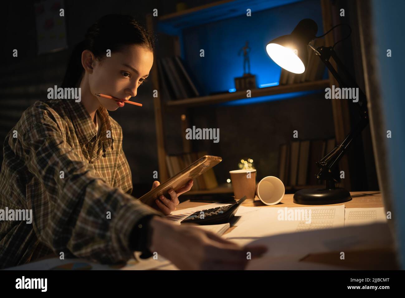 Schöne asiatische junge Mädchen mit Smartphone während des Studiums am Abend zu Hause. Bildung, Technologie, Überarbeit und Menschen Stockfoto