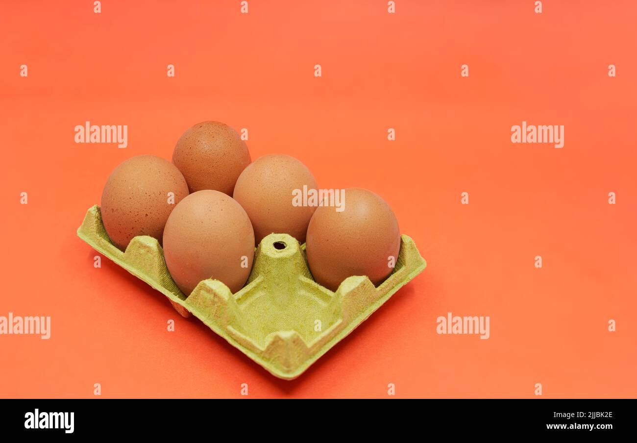 Fünf braune Eier statt sechs in einem offenen Eierkarton auf orangefarbenem Hintergrund. Shrinkflation-Konzept. Stockfoto