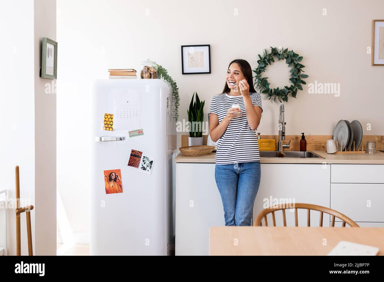 Hübsche junge Frau, die natürlichen Joghurt isst, während sie zu Hause in der Küche steht Stockfoto
