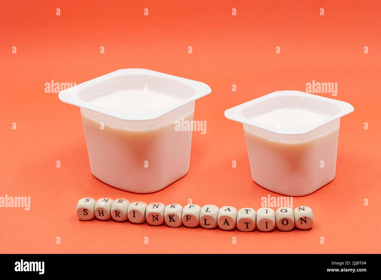Reduzierter Joghurt auf orangefarbenem Hintergrund. Inflation, Skimpflation oder Schrumpfung Konzept der weniger für den gleichen Preis. Stockfoto