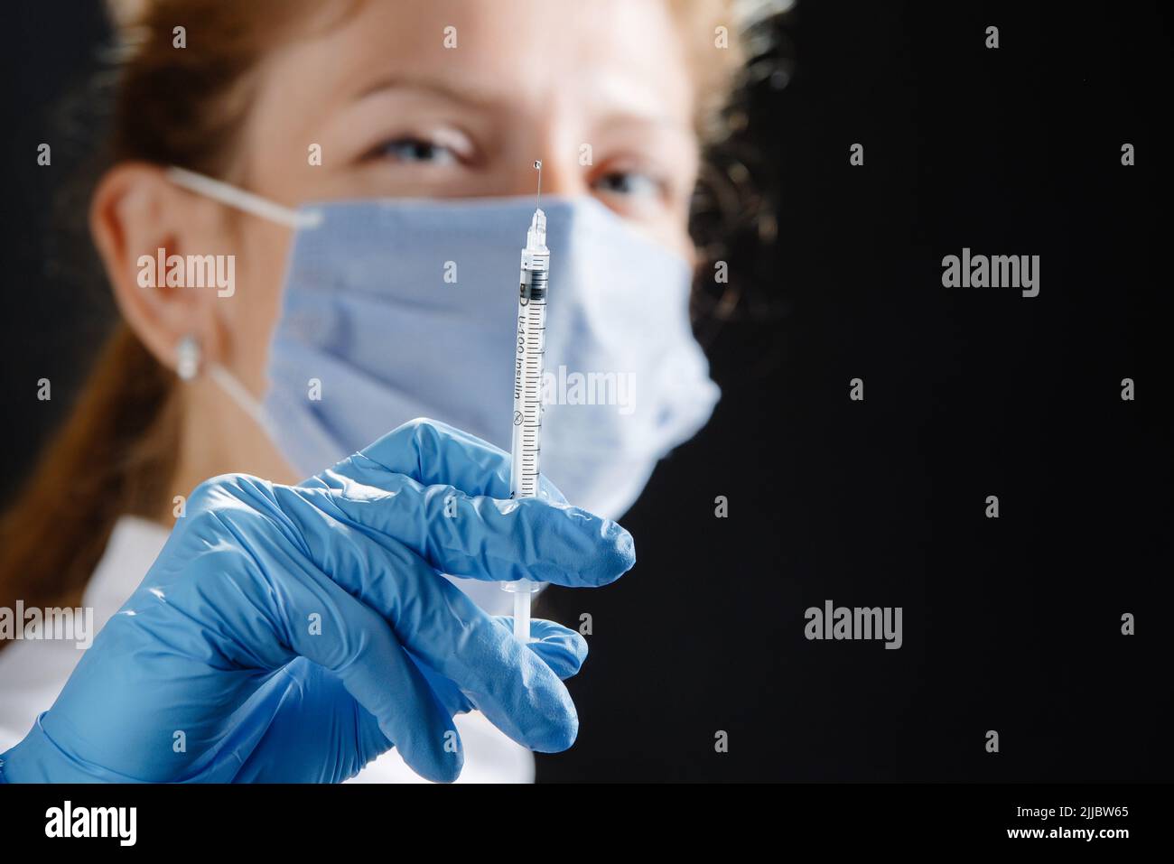 Eine junge Ärztin mit einer Spritze schaut auf die Kamera. Eine Krankenschwester, die eine medizinische Maske und blaue Latexhandschuhe trägt. Medizin und Gesundheitswesen. Impfung Stockfoto