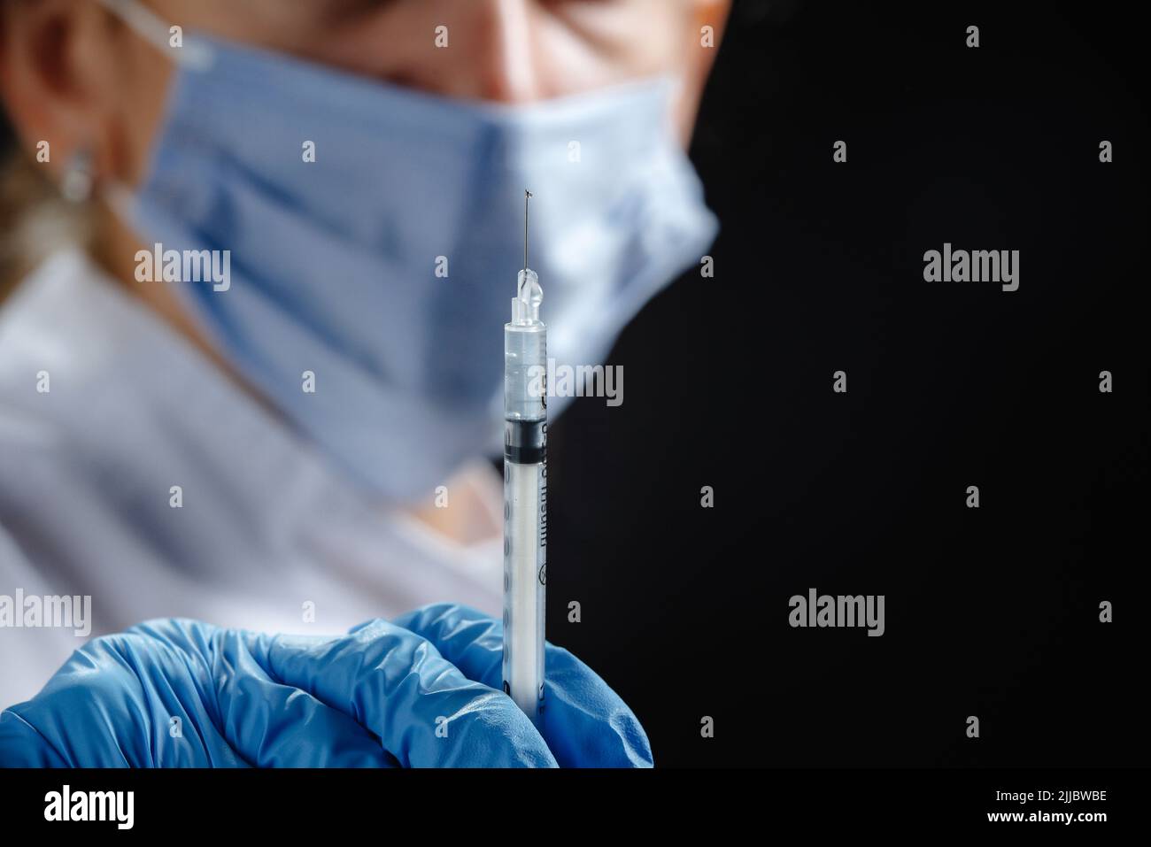 Eine junge Ärztin mit einer Spritze schaut auf die Kamera. Eine Krankenschwester, die eine medizinische Maske und blaue Latexhandschuhe trägt. Medizin und Gesundheitswesen. Impfung Stockfoto